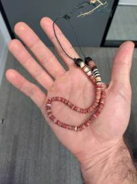 Item 3. In the palm of a hand, a short string of several rough red disks of varying shades, each end capped with a large shiny black bead and tied together in a frayed knot.